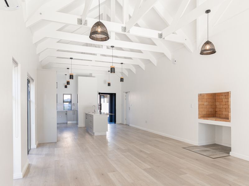 Spacious open-plan living area featuring high vaulted ceilings with exposed trusses, a built-in brick fireplace, and a modern kitchen with a central island.
