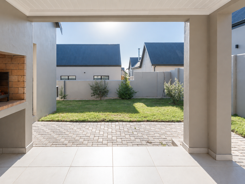 A covered patio featuring a built-in braai, tiled flooring, and direct access to a private paved area and garden.