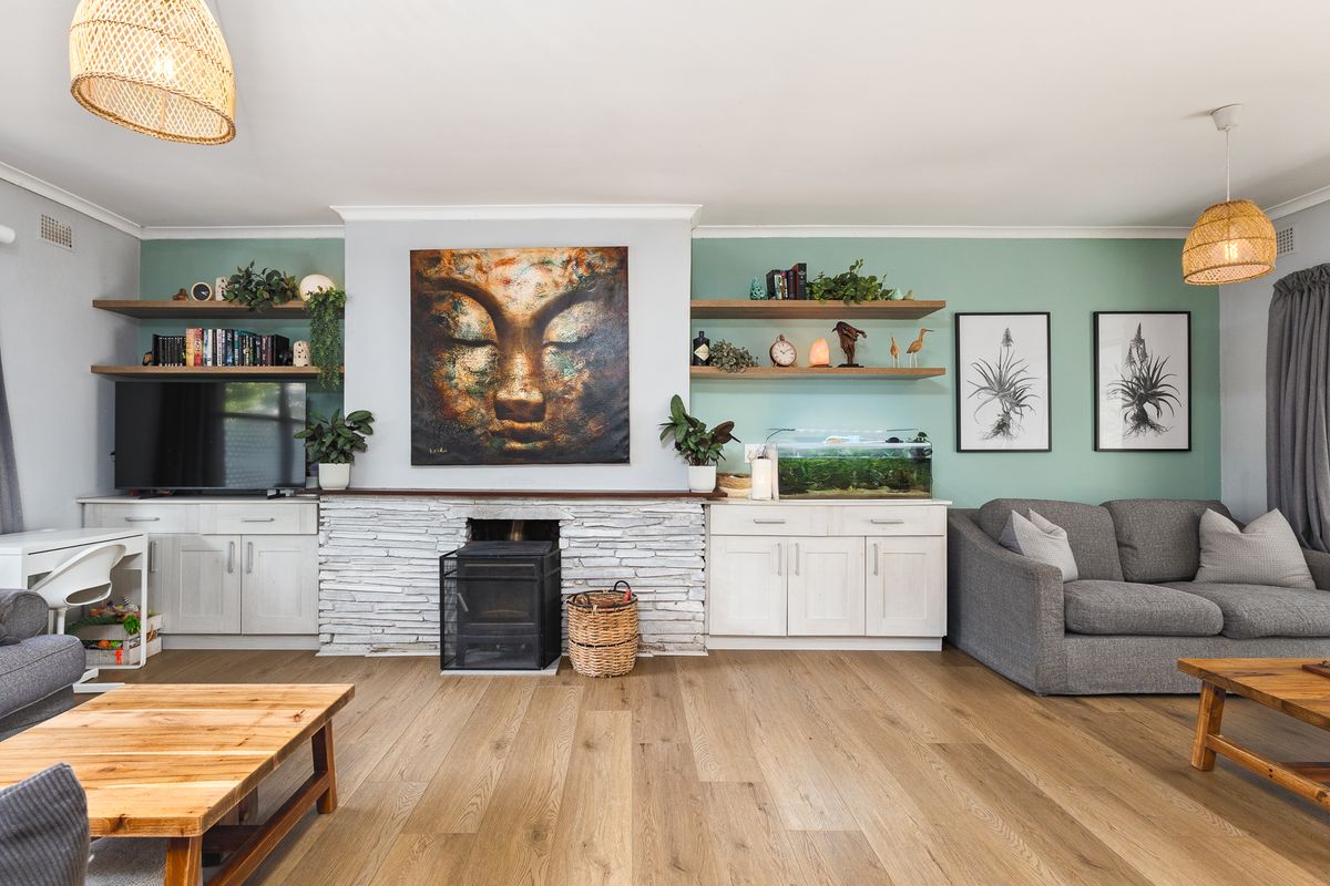 A well-maintained living room featuring a central stone-clad fireplace, built-in cabinetry, floating timber shelving, and modern timber flooring.