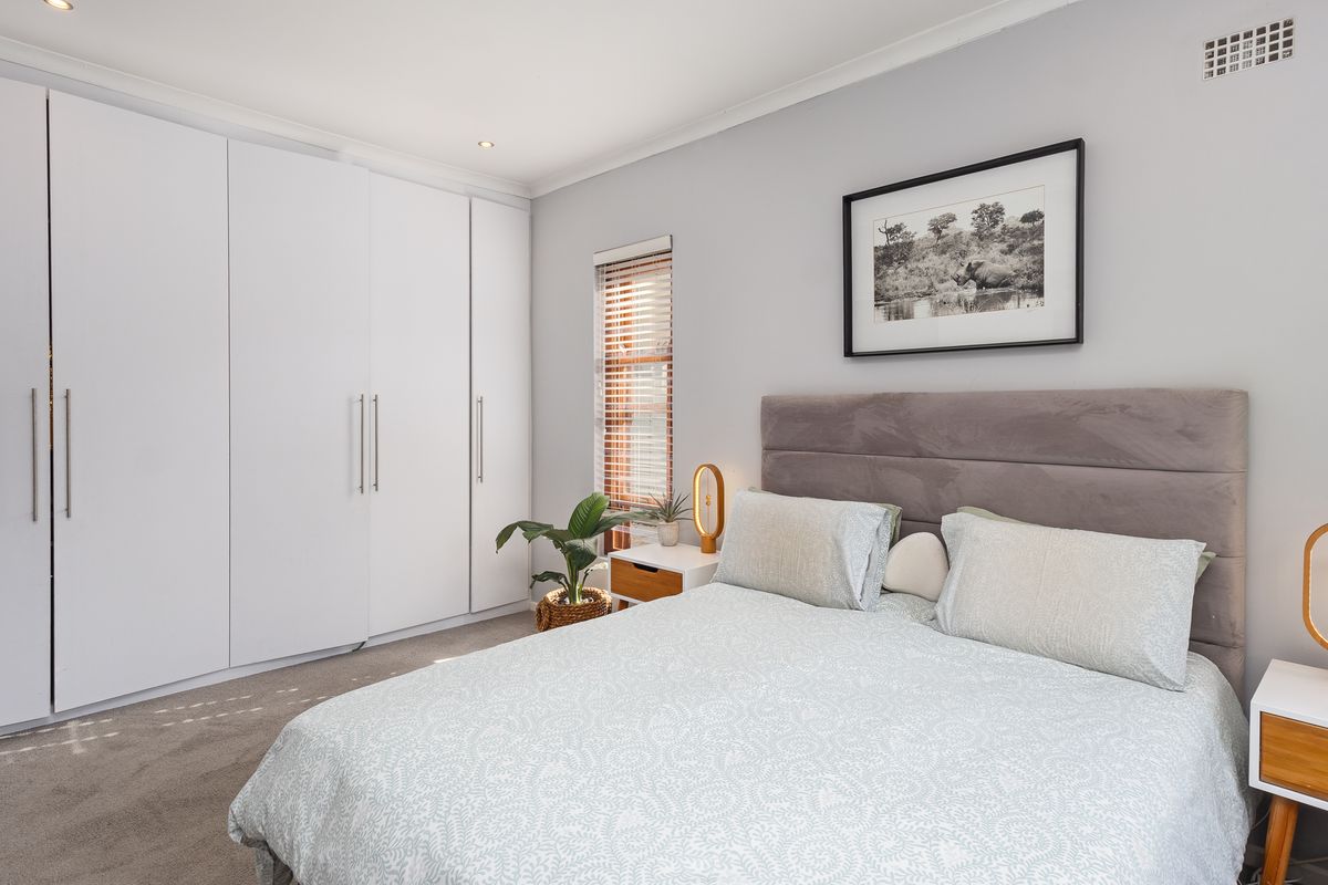 A well-maintained bedroom featuring neutral carpeting, built-in floor-to-ceiling cupboards, recessed lighting, and a window fitted with venetian blinds.
