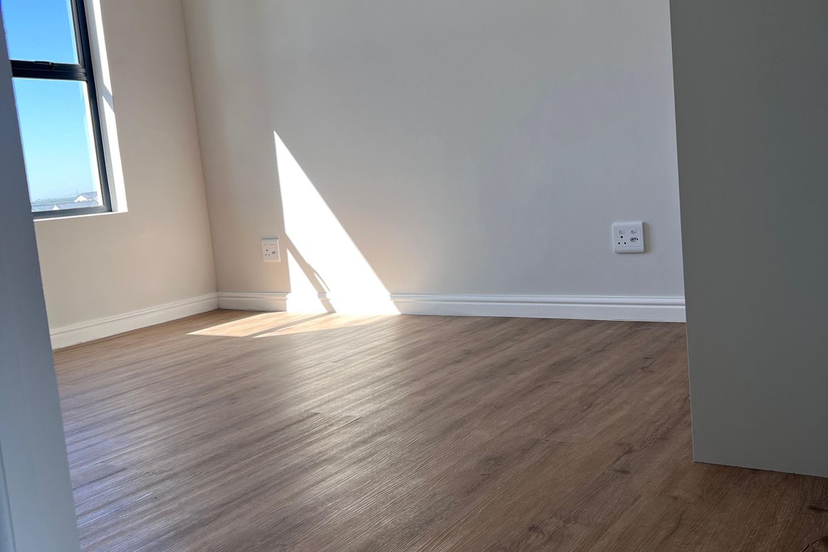 A bright, empty bedroom featuring modern laminate flooring, neutral walls, and a window with natural light.