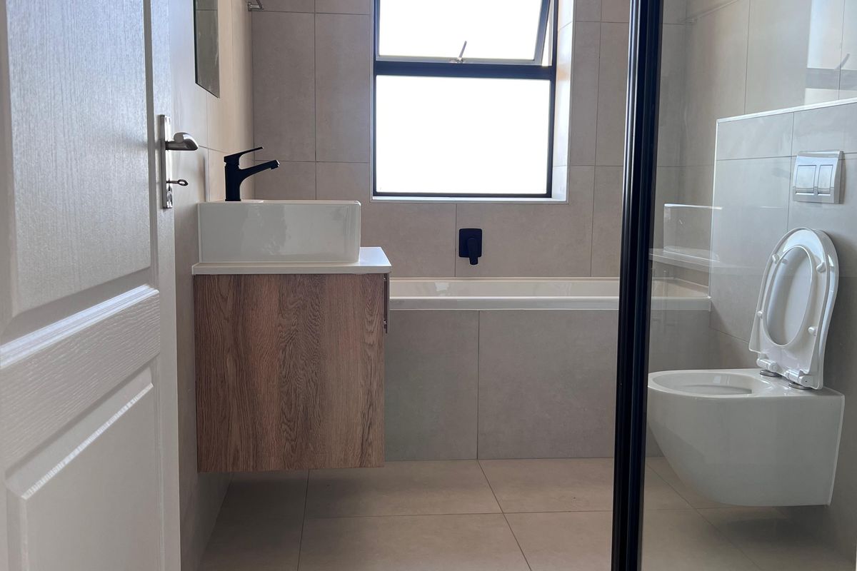 Modern bathroom featuring a wall-hung vanity with vessel sink, built-in bathtub, wall-hung toilet with concealed cistern, and a glass-enclosed shower.
