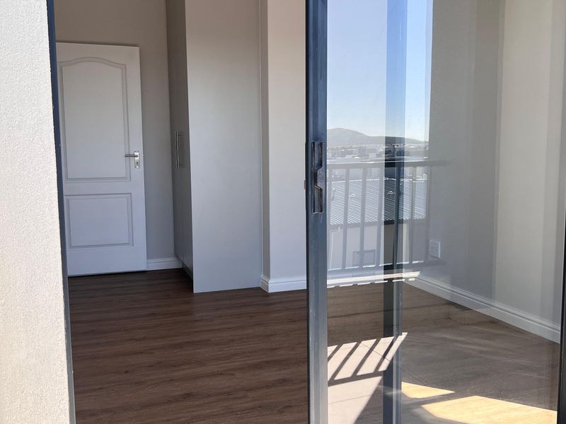 A bright, empty bedroom featuring modern laminate flooring, a built-in cupboard, and a large sliding glass door leading to an outdoor area.