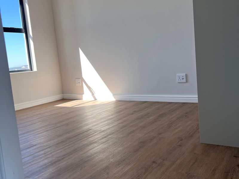 A bright, empty bedroom featuring modern laminate flooring, neutral walls, and a window with natural light.