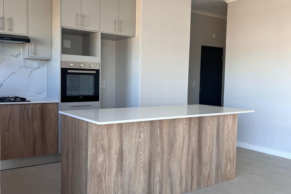 Modern kitchen featuring a central island, stone countertops, built-in oven, extractor fan, and sleek cabinetry with neutral tiled flooring.