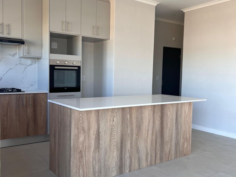 Modern kitchen featuring a central island, stone countertops, built-in oven, extractor fan, and sleek cabinetry with neutral tiled flooring.