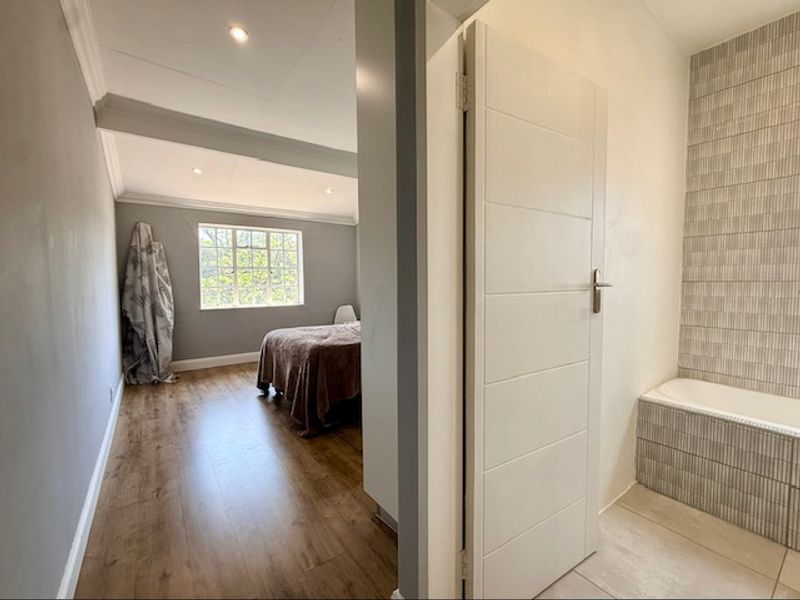 A view from a hallway looking into a bedroom, featuring laminate flooring, recessed lighting, and a bathroom with a tiled bathtub surround.