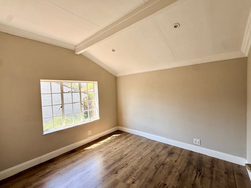 A bright, empty bedroom featuring laminate flooring, a vaulted ceiling with recessed lighting, and a classic grid window.
