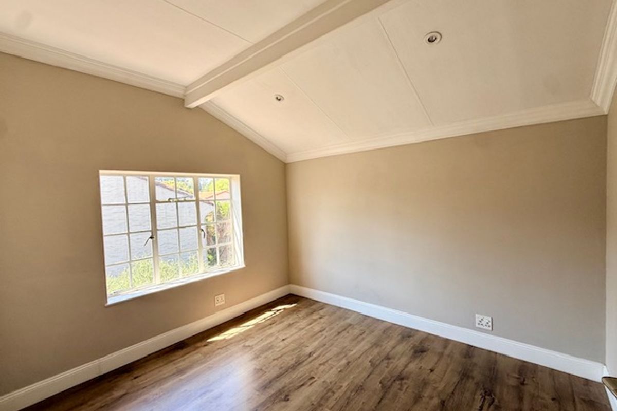 A bright, empty bedroom featuring laminate flooring, a vaulted ceiling with recessed lighting, and a classic grid window.