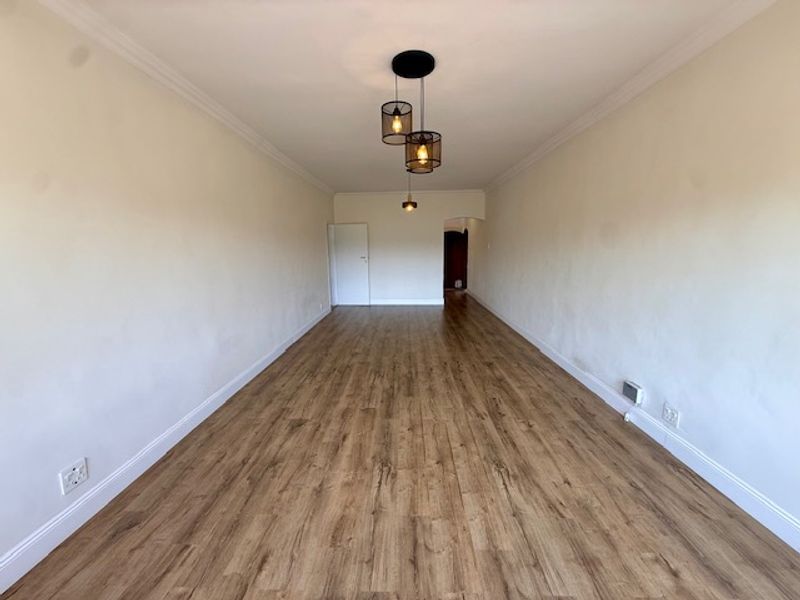 A spacious, empty living area featuring wood-look laminate flooring, neutral walls, and modern pendant lighting, ready for personalization.