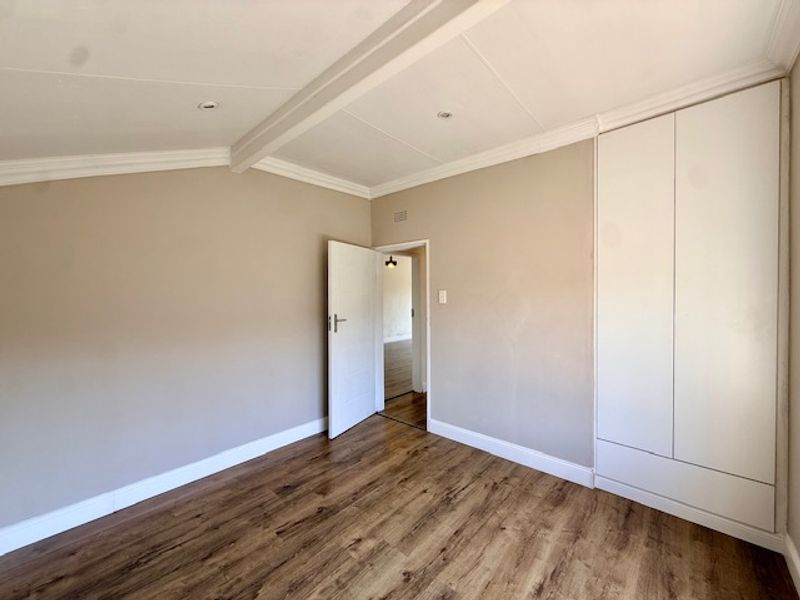 A bright, empty bedroom featuring laminate flooring, built-in cupboards, and recessed ceiling lighting with decorative coving.
