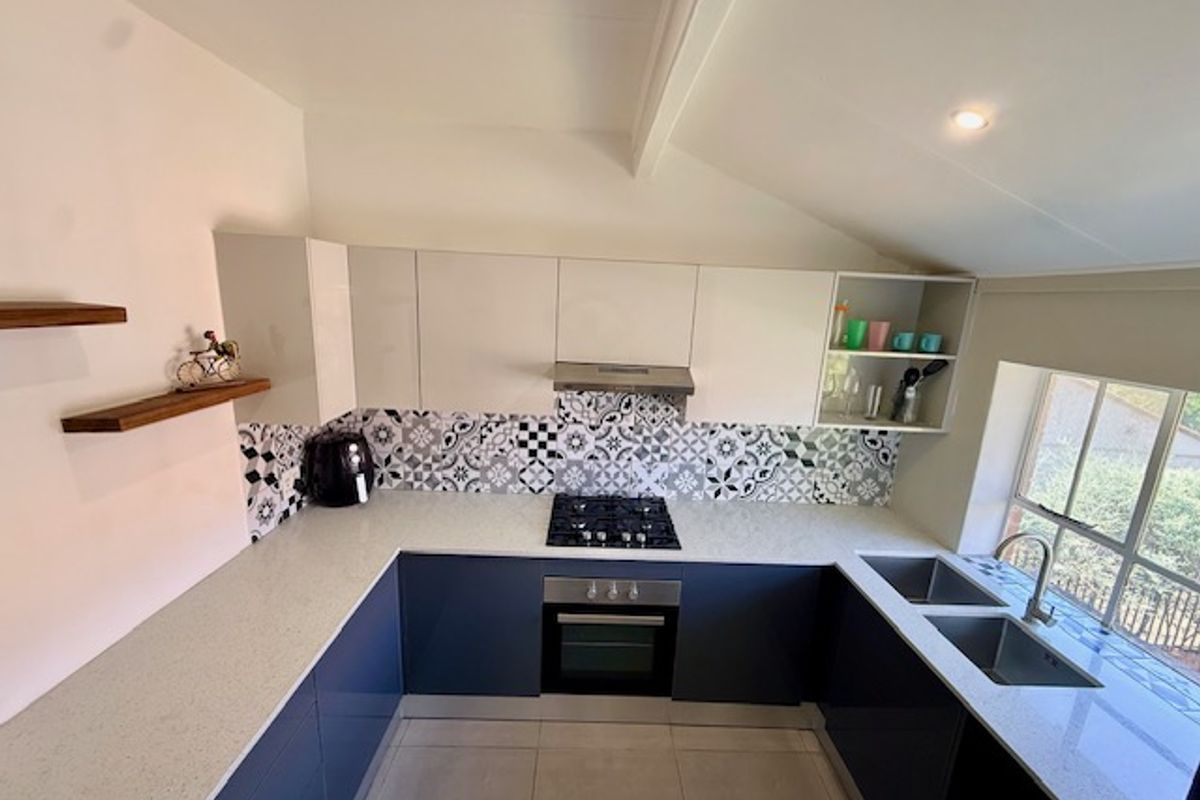 Modern U-shaped kitchen featuring high-gloss cabinetry, stone countertops, a gas hob with extractor, and a double basin sink under a sloped ceiling.