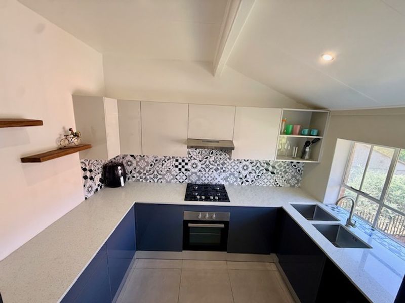 Modern U-shaped kitchen featuring high-gloss cabinetry, stone countertops, a gas hob with extractor, and a double basin sink under a sloped ceiling.