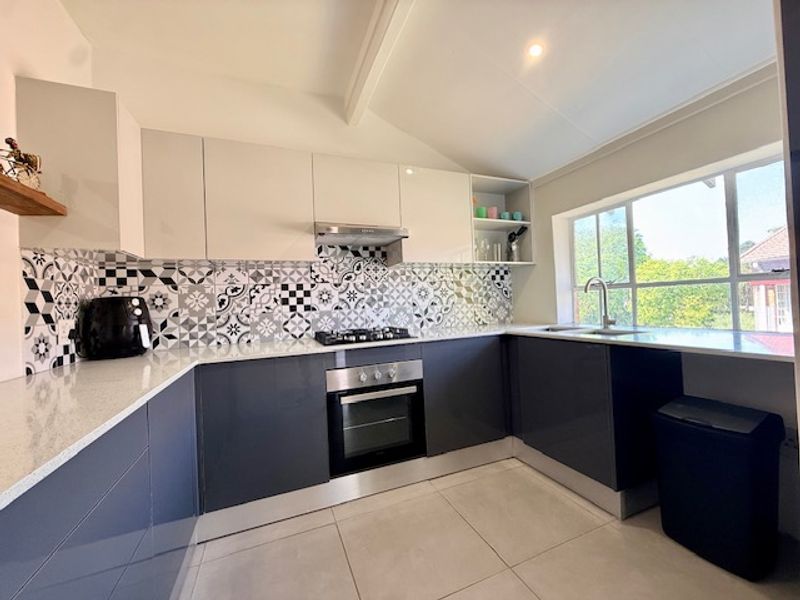 Modern kitchen featuring high-gloss cabinetry, quartz countertops, a gas hob with extractor, and a striking patterned tile backsplash with ample natural light.