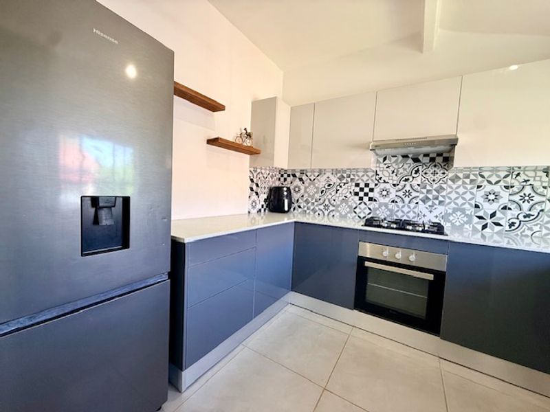 Modern kitchen featuring sleek gloss cabinetry, quartz countertops, a gas hob with extractor fan, and a decorative patterned tile backsplash.