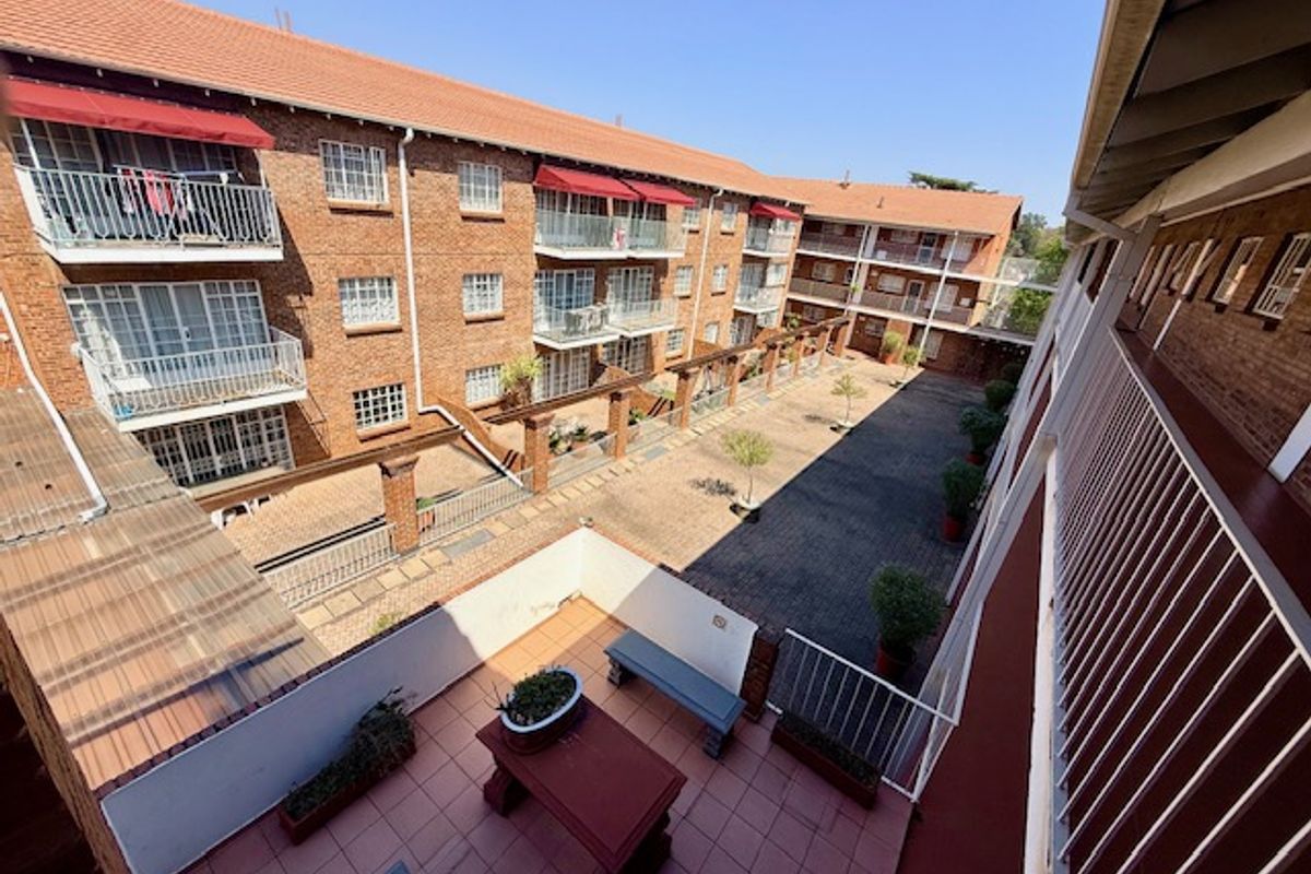 An elevated view of an apartment complex courtyard featuring brick facades, tiled roofs, and private balconies overlooking a paved communal area.