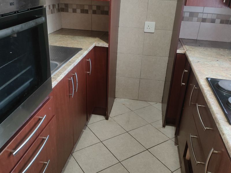 A compact kitchen featuring dark wood-look cabinetry, stone-effect countertops, a built-in oven, and an electric hob with tiled backsplash and flooring.