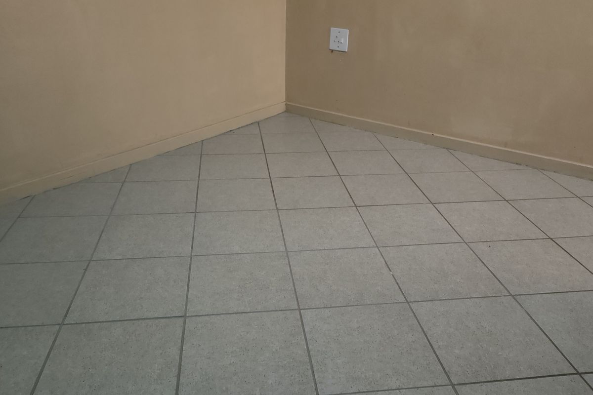 An empty room corner featuring neutral painted walls, ceramic floor tiling, and a standard electrical outlet.