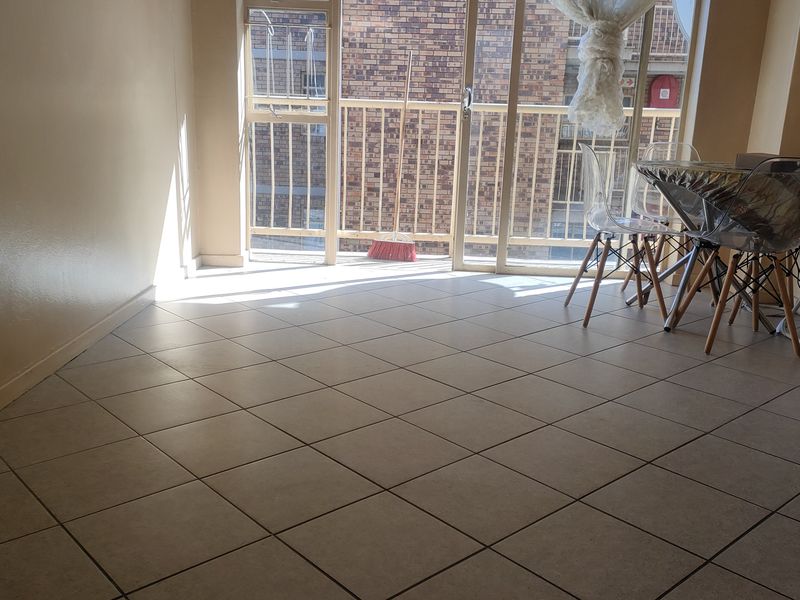 A living area featuring neutral tiled flooring and a large sliding glass door providing access to a balcony.