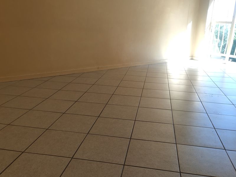 An empty living room featuring neutral tiled flooring and a sliding glass door providing natural light and access to the balcony.