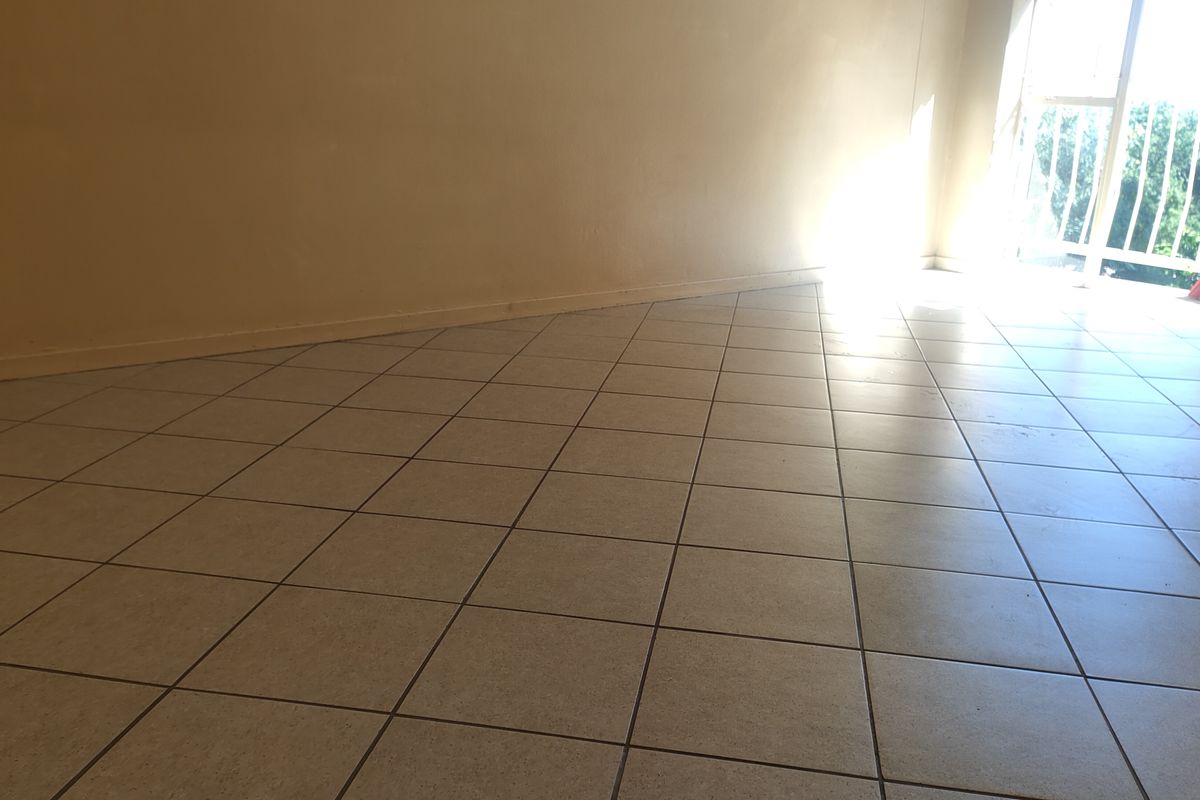 An empty living room featuring neutral tiled flooring and a sliding glass door providing natural light and access to the balcony.