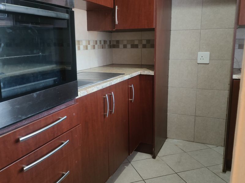 A functional kitchen featuring built-in cabinetry, a wall-mounted oven, laminate countertops, and tiled flooring with a neutral backsplash.
