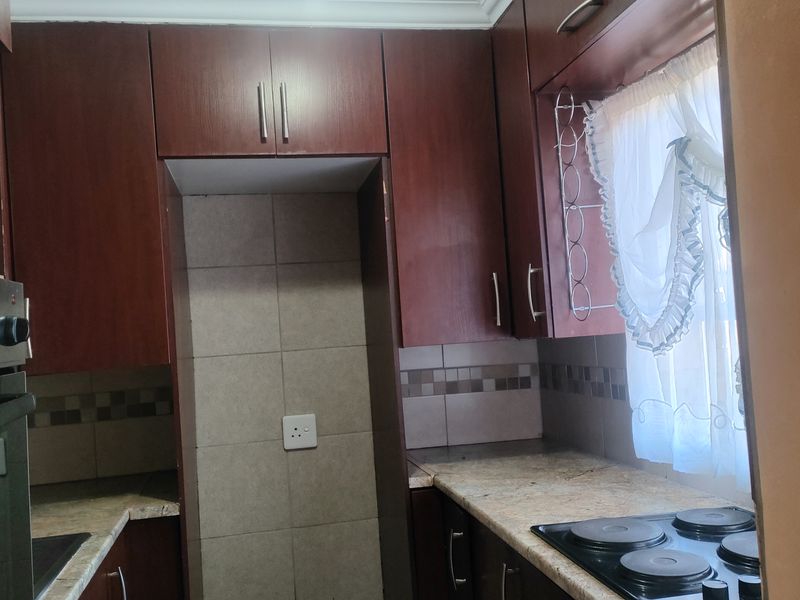 A functional kitchen featuring dark wood cabinetry, granite countertops, a built-in oven, and an electric hob with a tiled backsplash.