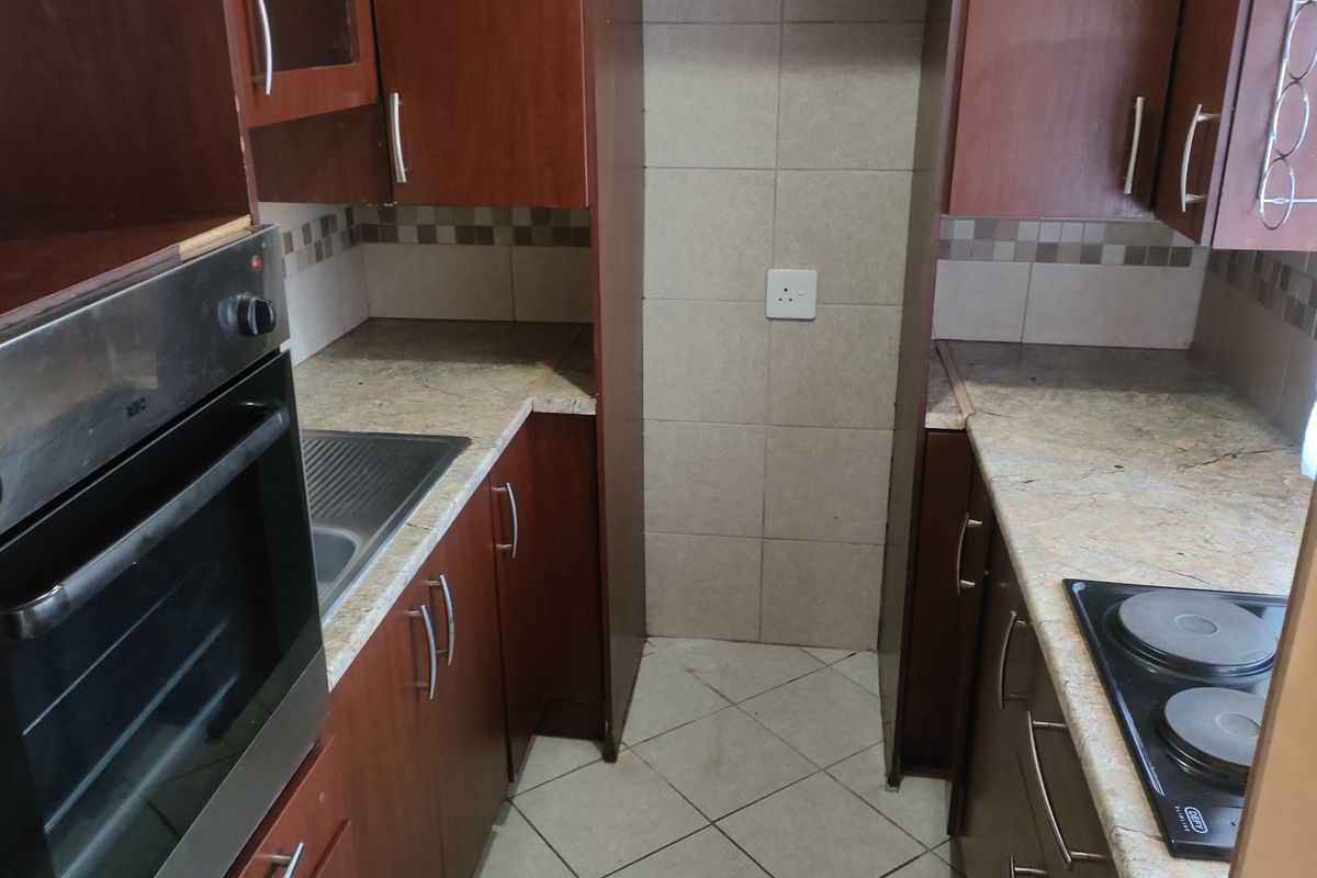 A compact kitchen featuring built-in wooden cabinetry, granite countertops, a stainless steel sink, and integrated cooking appliances with tiled finishes.
