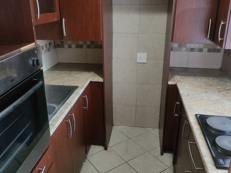 A compact kitchen featuring built-in wooden cabinetry, granite countertops, a stainless steel sink, and integrated cooking appliances with tiled finishes.