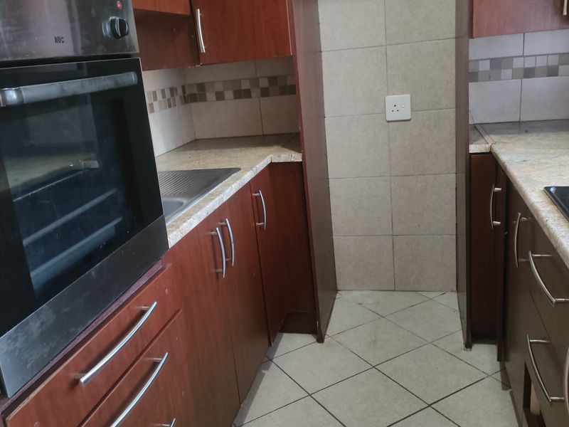 A compact kitchen featuring built-in cabinetry, a wall-mounted oven, a hob, and tiled finishes, offering a functional layout ready for modernization.