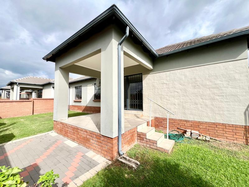 A rear view of the townhouse featuring a covered patio with tiled flooring, brick base detailing, and a paved walkway leading to the garden.