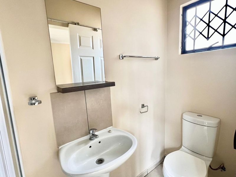 A clean and functional bathroom featuring a pedestal basin, toilet, wall-mounted mirror, and security bars on the window.