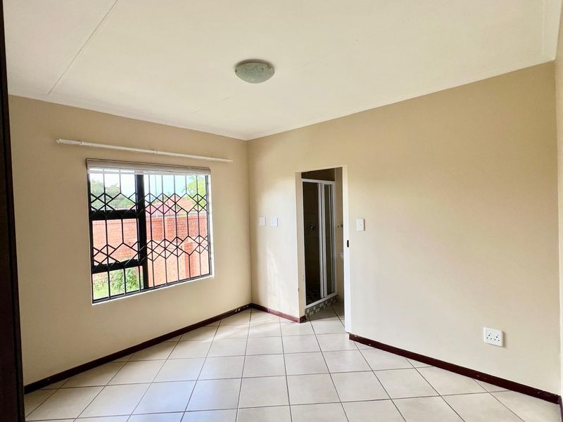 A clean, empty bedroom featuring tiled flooring, a security gate on the window, and an adjoining en-suite bathroom entrance.