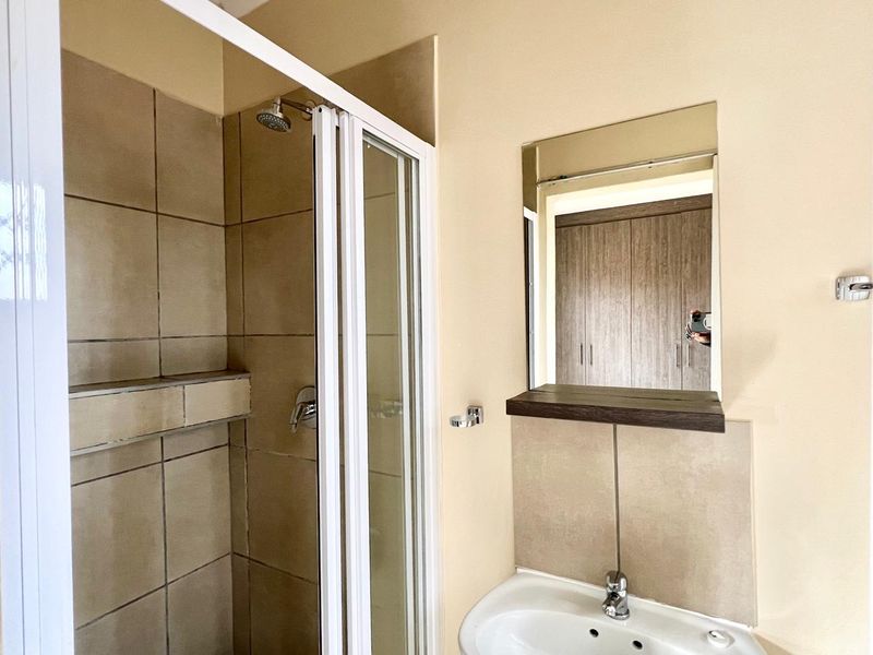 A clean and functional bathroom featuring a tiled shower enclosure, pedestal basin, and wall-mounted mirror.