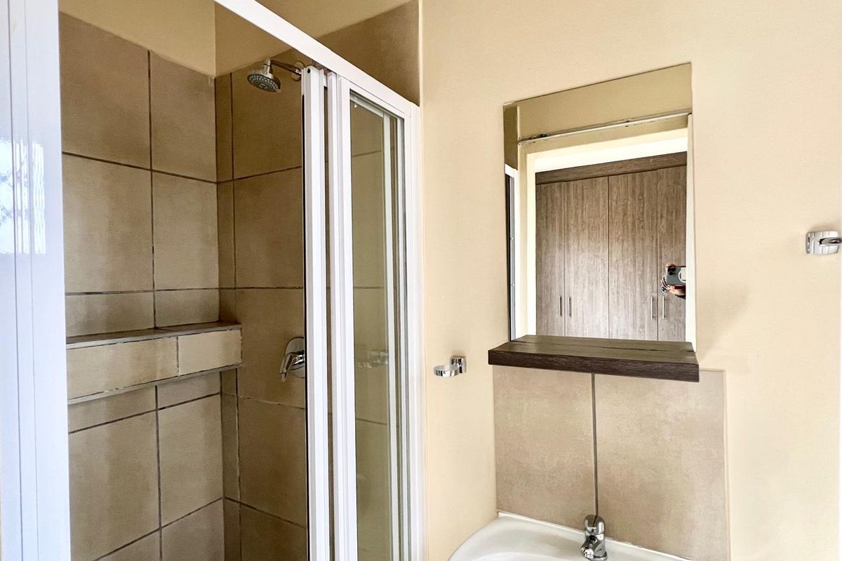 A clean and functional bathroom featuring a tiled shower enclosure, pedestal basin, and wall-mounted mirror.