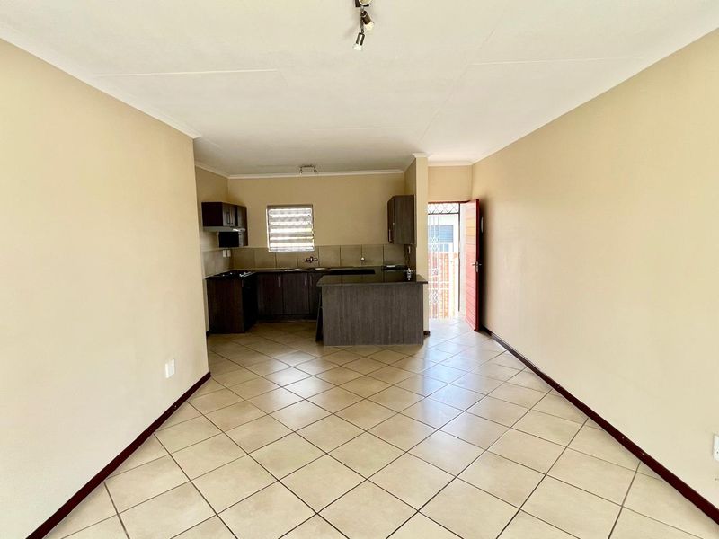 An open-plan living and kitchen area featuring tiled flooring, dark wood cabinetry, and a kitchen island, leading to an exterior entrance.