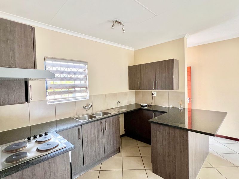 Modern kitchen featuring dark wood cabinetry, granite countertops, an electric hob with extractor, and neutral tiled flooring in a clean, open-plan layout.