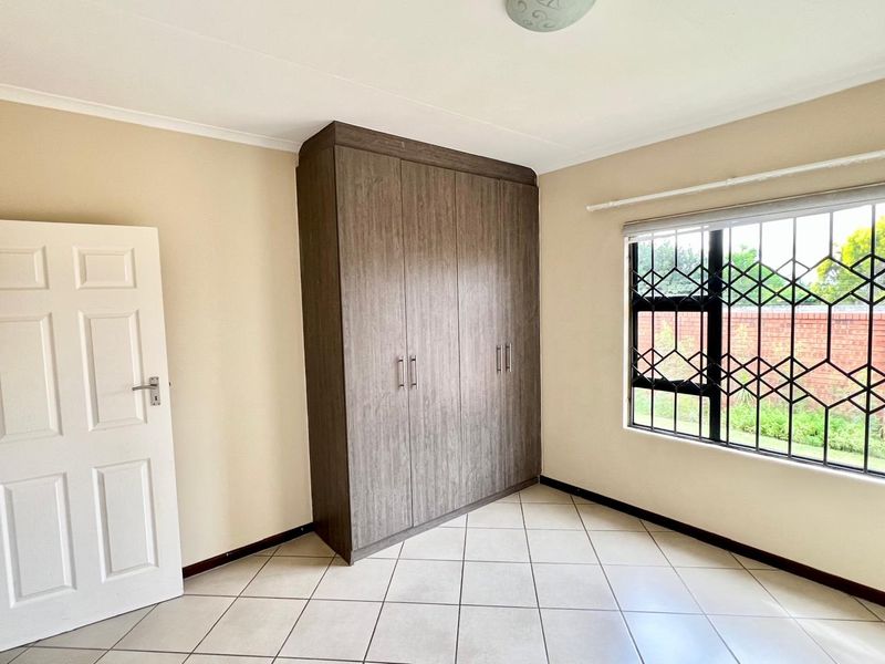 A bright, empty bedroom featuring neutral tiled flooring, a large built-in wooden wardrobe, and windows fitted with security bars.