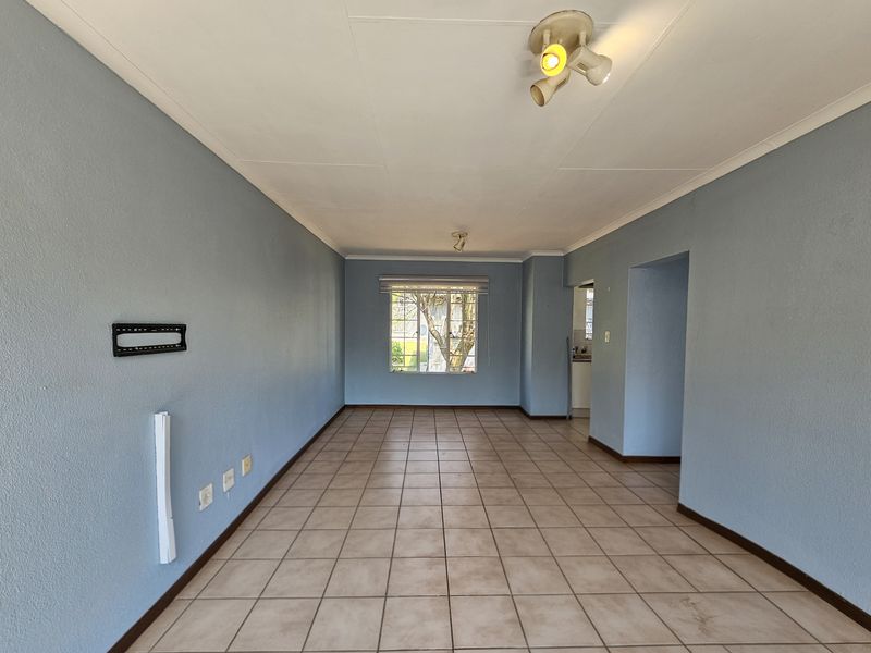 A spacious, empty living area featuring neutral tiled flooring, coved ceilings, and natural light from a rear-facing window.
