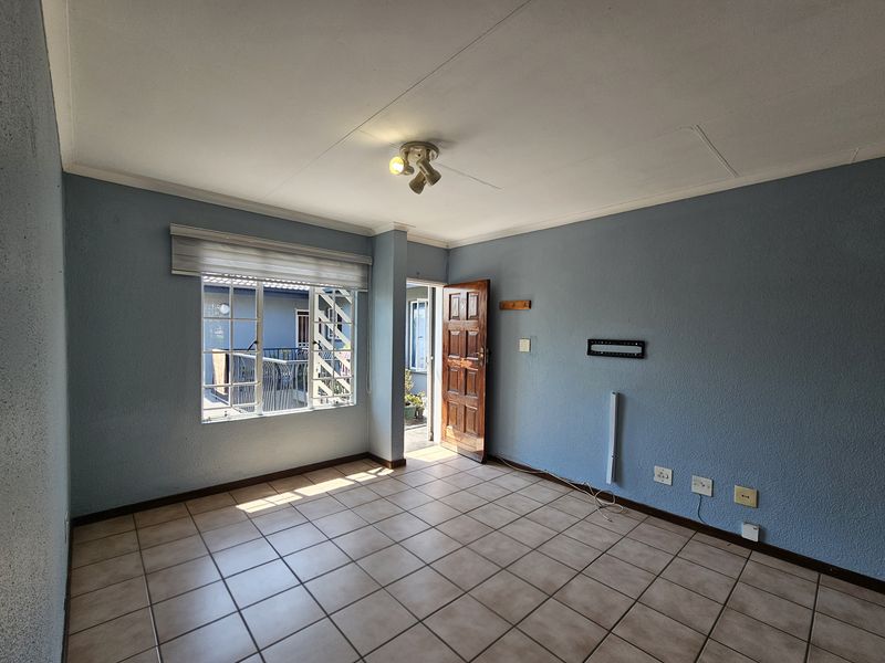 An empty living room featuring tiled flooring, blue textured walls, and a timber entrance door, providing a blank canvas for interior design.