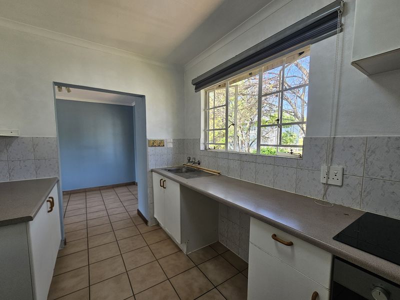 A functional kitchen featuring built-in cabinetry, laminate countertops, a stainless steel sink, and integrated cooking appliances, finished with ceramic tile flooring and backsplash.