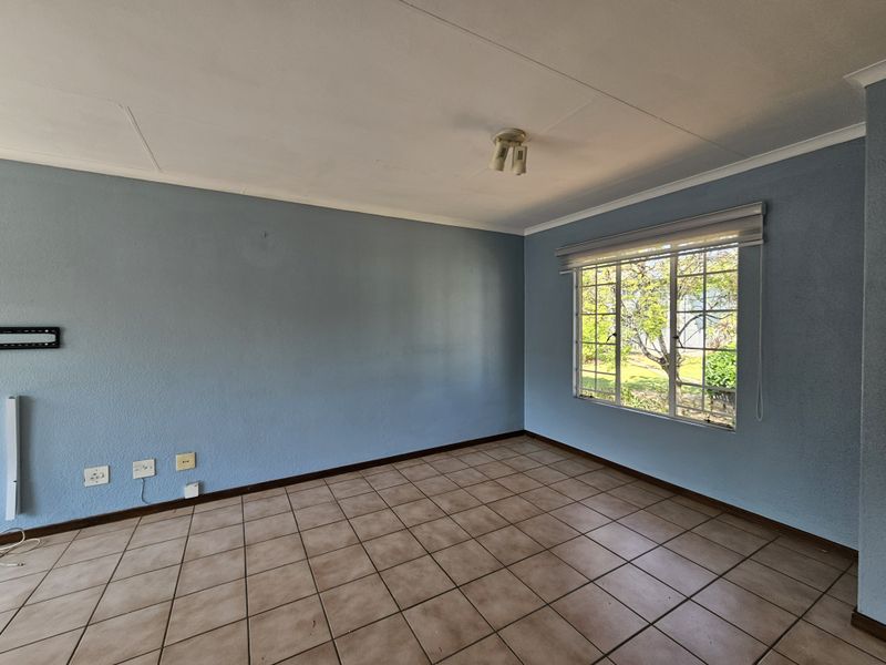 An empty living room featuring ceramic floor tiles, blue painted walls, and a window with security bars and a roller blind.