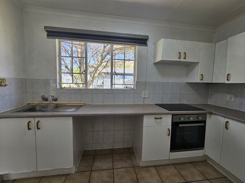 A functional kitchen featuring white built-in cabinetry, laminate countertops, a built-in oven and hob, and tiled flooring with a window view.