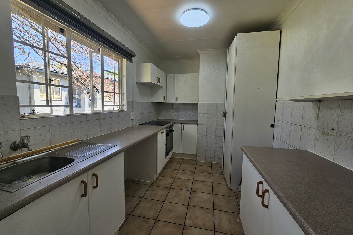 A functional, empty kitchen featuring built-in cabinetry, laminate countertops, a built-in oven with hob, and tiled flooring throughout.