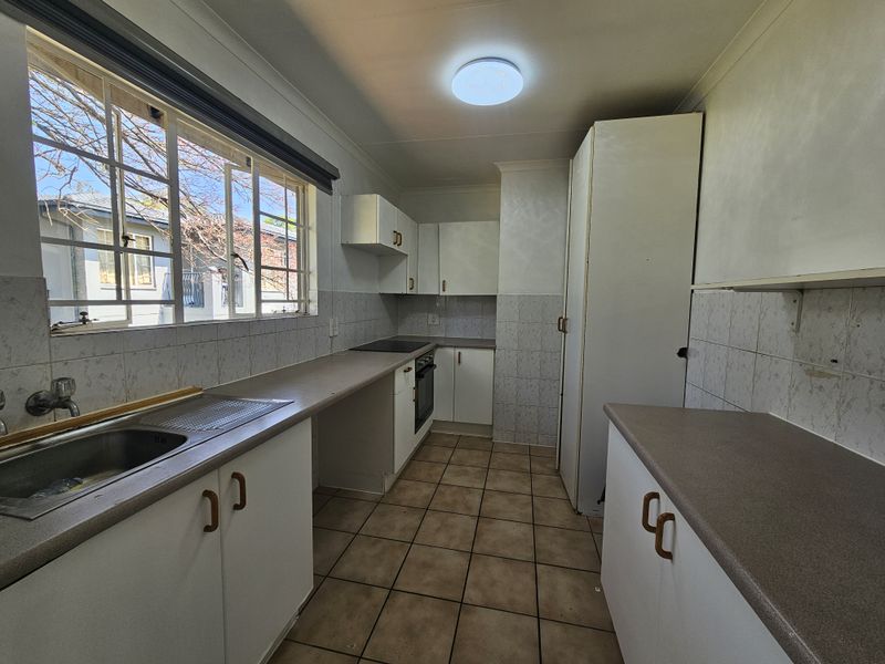 A functional, empty kitchen featuring built-in cabinetry, laminate countertops, a built-in oven with hob, and tiled flooring throughout.