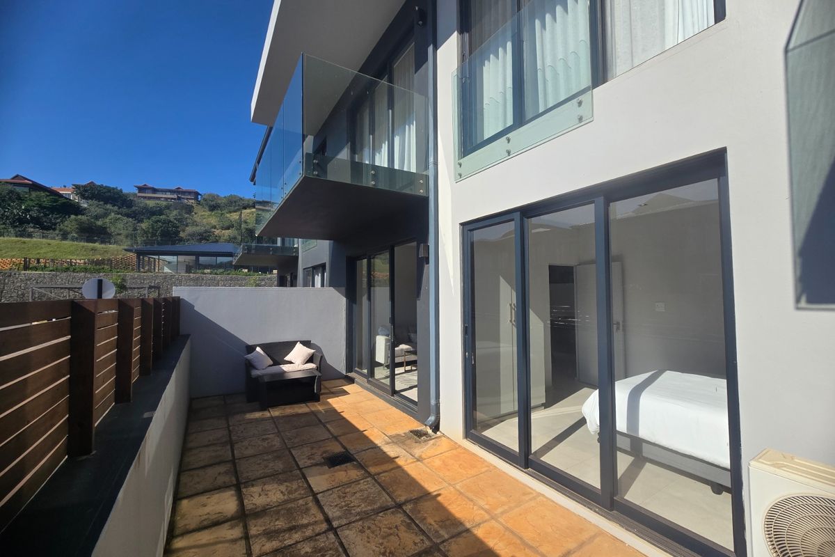 A ground floor patio area featuring tiled flooring, glass sliding doors, and a timber privacy screen, providing access to the apartment interior.