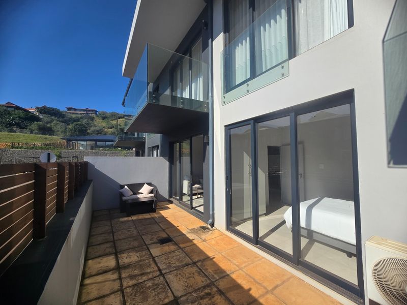 A ground floor patio area featuring tiled flooring, glass sliding doors, and a timber privacy screen, providing access to the apartment interior.