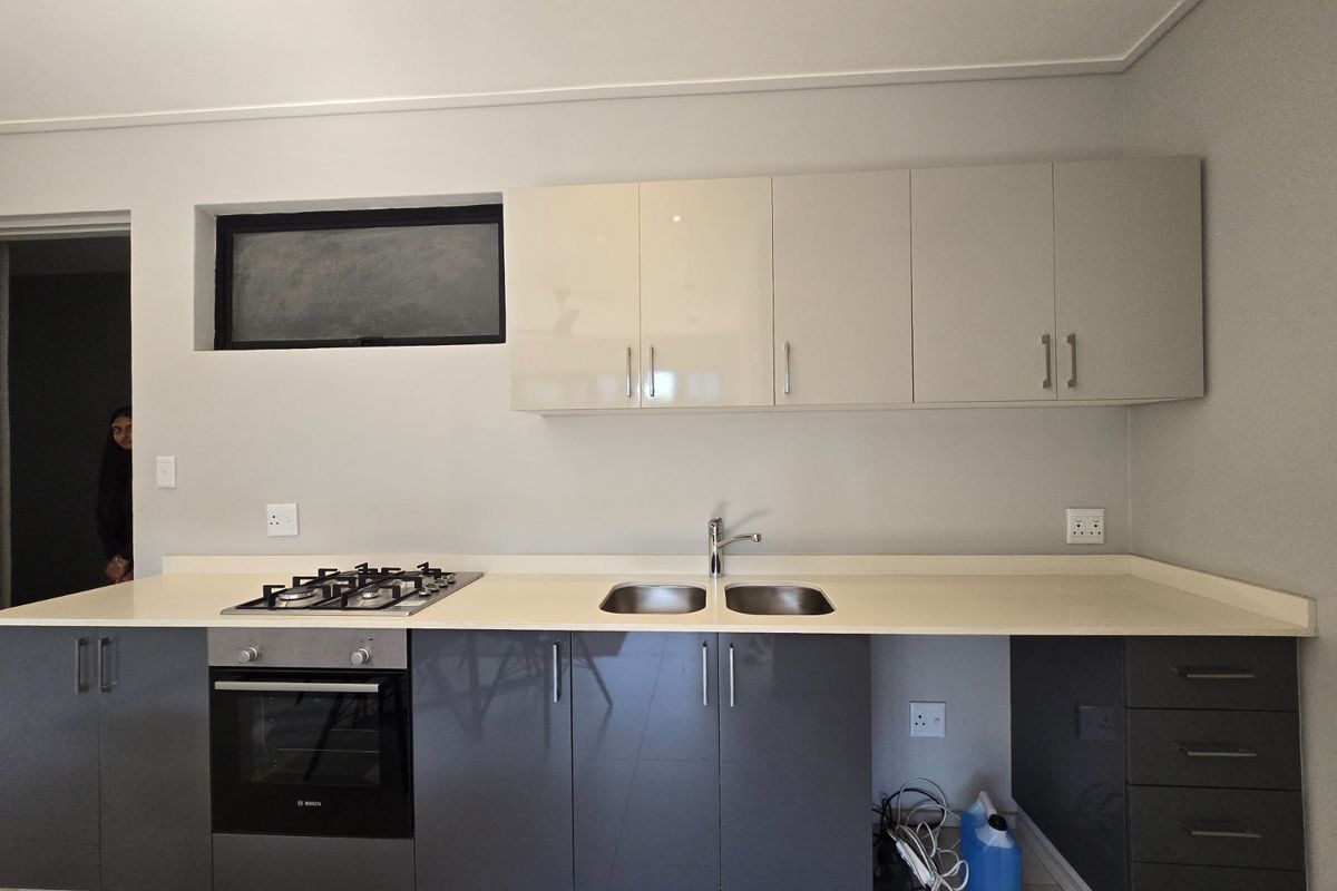 Modern kitchen featuring sleek grey and cream cabinetry, stone countertops, a built-in gas hob, oven, and a double sink with a mixer tap.