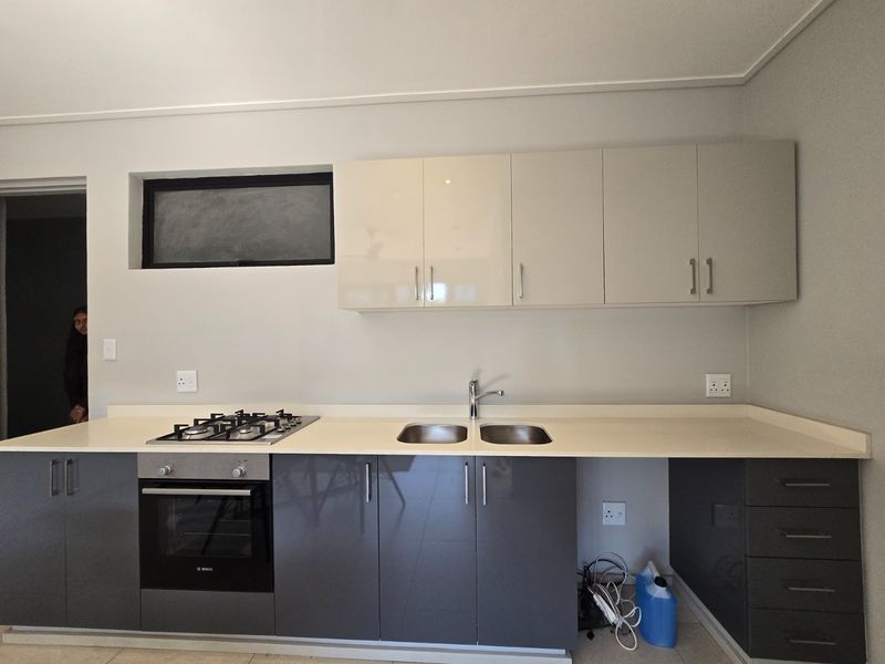 Modern kitchen featuring sleek grey and cream cabinetry, stone countertops, a built-in gas hob, oven, and a double sink with a mixer tap.
