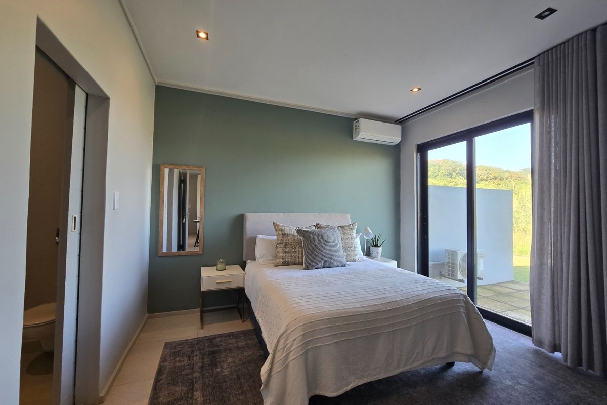 A modern bedroom featuring a sage green accent wall, split-system air conditioning, and large sliding glass doors providing access to an outdoor area.
